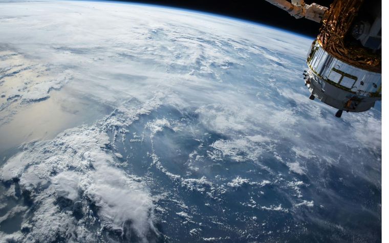 Blick aus dem Orbit auf die bewölkte Erde, am rechten Bildrand ein Satellit.