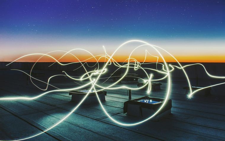 Leuchtende Lichtspuren wie fließende Energie über einem Flachdach in der Dämmerung.
